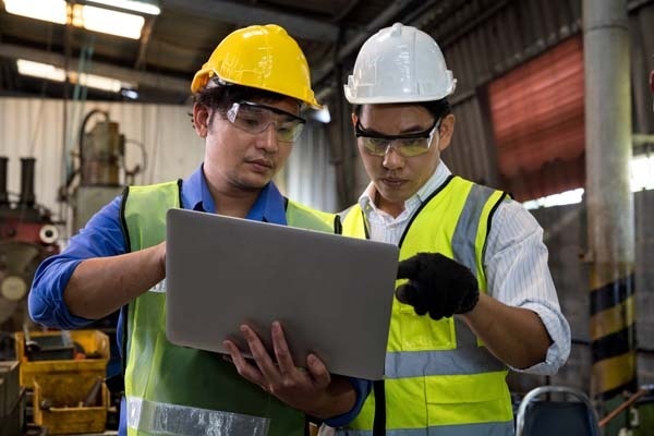 Two men in hard hats looking at a computer